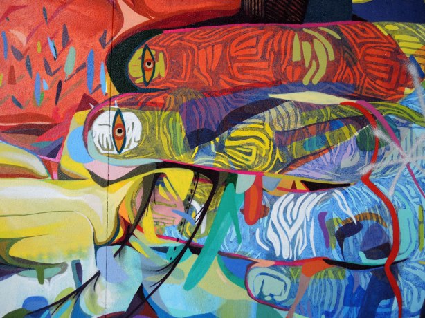 Close up of graffiti painted fingers in many bright colours.  They are very large.  Each fingernail has an eye.