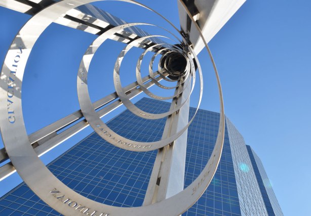 Looking up inside a sculpture that is a ribbon of stainless steel that winds up a conical hape, supported on 4 sides by stainless steel bars.