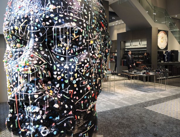 A large (about 6 foot tall) black head sits in the front of a menswear store. People have been encouraged to add chewed wads of gum to the head. It is about one third covered.