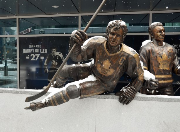 A bronze statue of Toronto Maple Leaf hockey player Darryl Sittler as he jumps over the boards and onto the ice, hockey stick in hand 