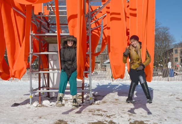 Two women sitting on the orange sling swings on a cold winter day at the beach