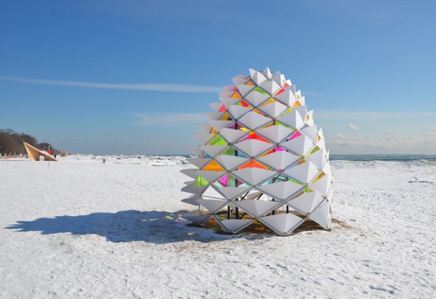 Art installation that looks like a giant white pinecone on the beach in winter.  The inside of the parts of the cone are bright translucent coloured plexiglass