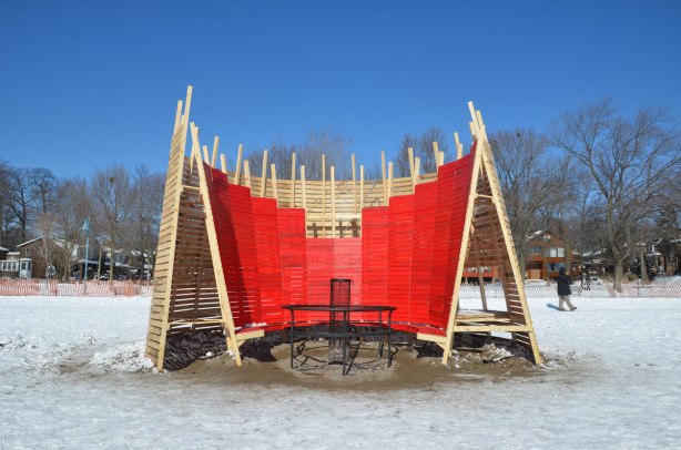 wooden structure on the beach in winter.   Part in painted red.  It is supposed to be a large chair, semi-circle, can seat a number of people. 