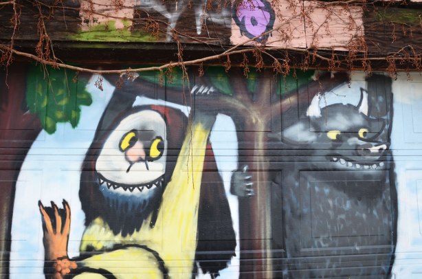 Close up of a Mural on a garage door of Max and the Wild Things, characters from the children's book "Where the Wild Things Are" .  Two of the wild things are  are swinging from tree branches. 