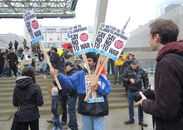 A man is handing out protest signs that say "Say no to Islamophobia"