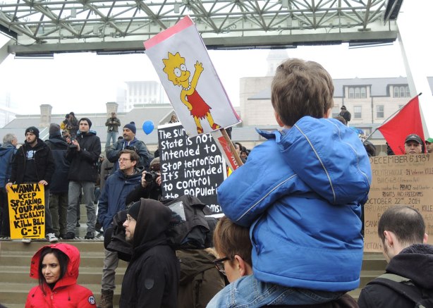 A boy on his mother's shoulders is holding a sign with a picture of Lisa on it.