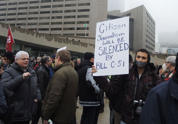 People at a protest rally.  One man has duct tape over his mouth and he is holding a placard that says "Citizen journalism will be silenced by Bill C-51"