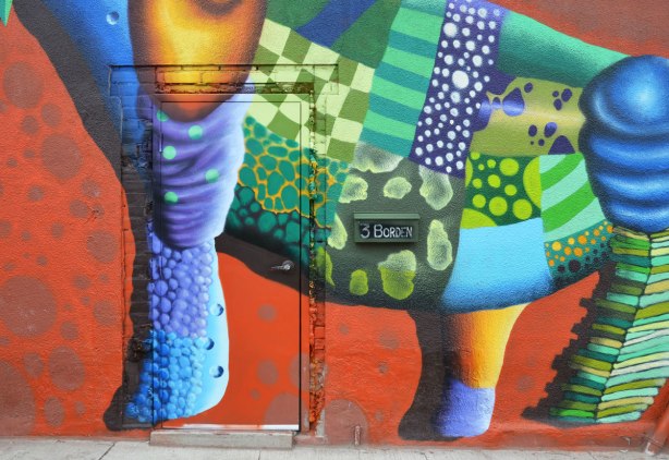 birdo street art, close up of multicoloured creature over a doorway.  Belly and legs are visible in the photo
