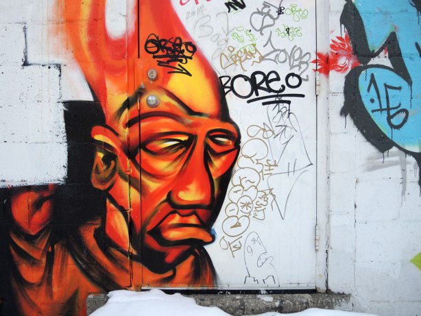 large stylized man's face graffiti in orange hues on a light grey door.  
