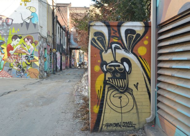 light brown poser bunny in Graffiti Alley - about 30 cm wide and 75 cm high on a wall that is perpendicular to the alley, Graffiti Alley is in the background.  Signed ambcrew 2014 
