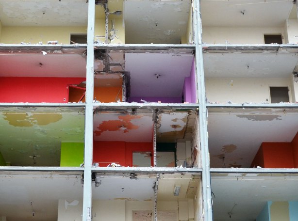 View of the interior of some of the apartments that were exposed when the exterior brick was removed.  Some of the rooms are painted in bright colours, purples, pinks and greens. 
