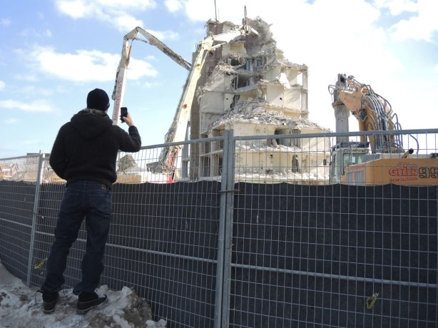 A man is taking a picture of a demolition in progress of an apartment building. 