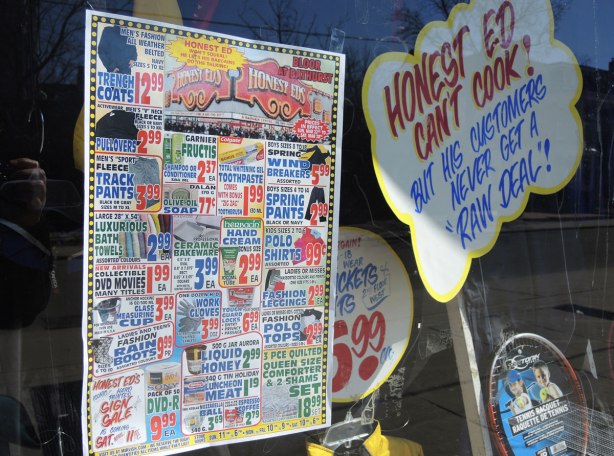 Signs in a store window.  One says "Honet Ed can't cook but his customers never get a raw deal" and the other is a page showing all the special prices available at the store.  It is printed like a newspaper page and there is a lot of information on it. 