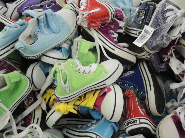 A bin full of brightly coloured kids running shoes in greens, blues, reds, etc