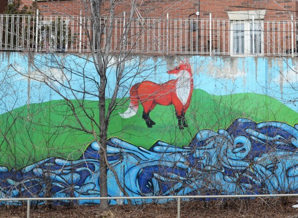 Part of a mural showing a fox standing beside a creek.  A bare tree is in front of the mural