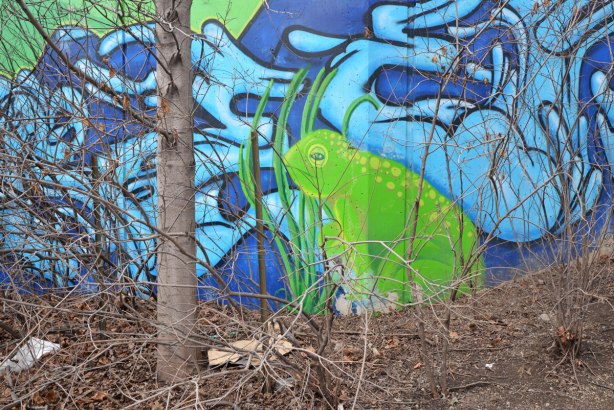 Part of a mural showing a large green frog sitting beside a creek.  A tree with no leaves is in front of the mural 