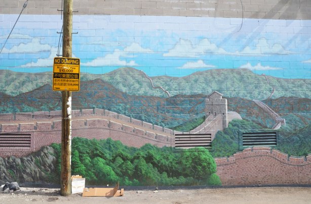 part of large mural of the great wall of China in an alley with a telephone pole in front of it. 