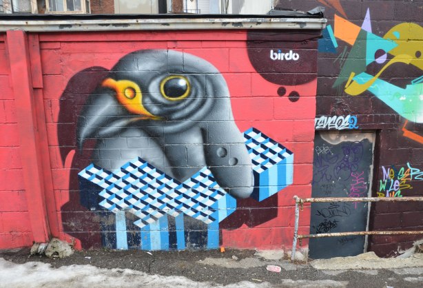 a mural by birdo, a small black and grey bird that is holding a geometric shape in blue and white diamond shaped sections. 