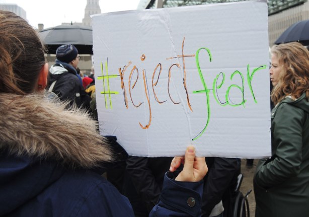 A protester is holding a hand written sign that says #rejectfear