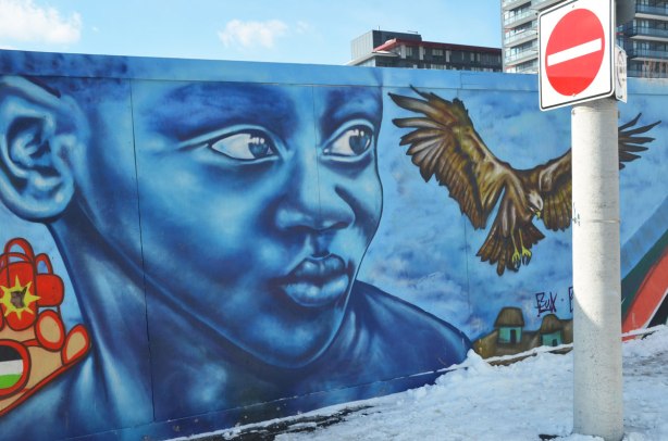 Colourful graffiti on hoardings around a construction site. Large blue boy's face with a large bird taking flight beside him