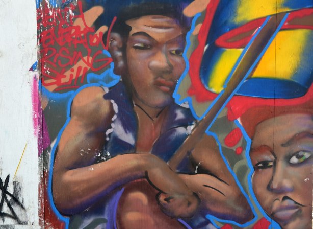 Street art painting of two guys on a wall around a construction site. There are words in the picture. The first word ends with e n c h I think. The other words are Generation Rising Still