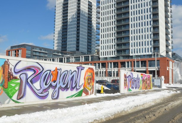 Colourful graffiti on hoardings around a construction site. The words Regent Park are written in large blue & purple cursive writing. An entrance to the construction site is between the two words.