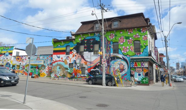 Looking across a city intersection to a store on the corner that has a large mural painted on the side of it.  Many Japanese motifs, many colours too. 