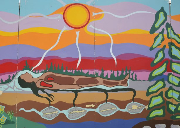 part of a First Nations story/legend themed mural painted on wood construction hoardings in Allan Gardens - the sun shones on a person lying on the ground. 