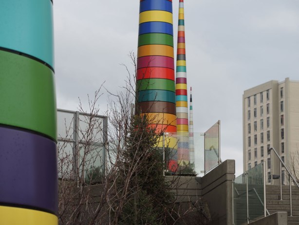 Four tall striped poles designed by Douglas Coupland as a public art installation.  The pole in the foreground, spring, can only be partially seen.  The winter pole is in the distance.  