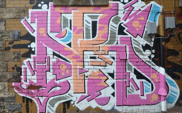 pink and pale orange graffiti tag painted on a brick wall in a Toronto alley