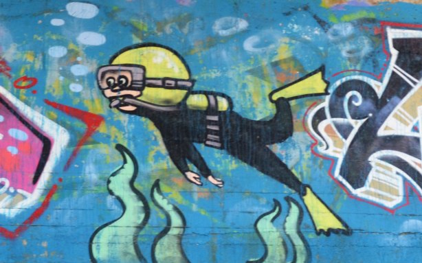 graffiti painting of a scuba diver swimming under water, under a bridge 