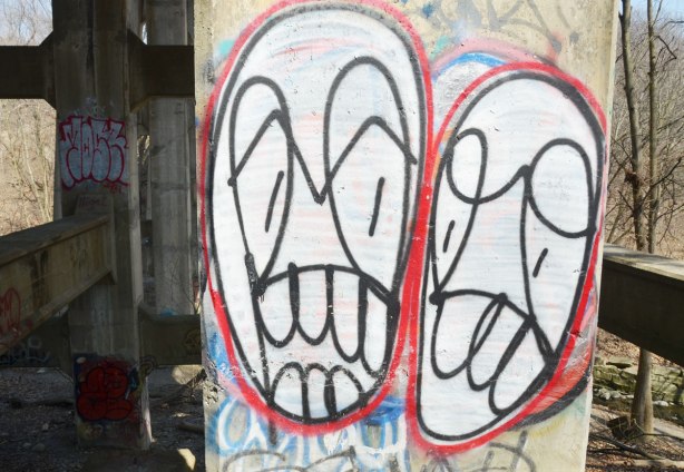 Two large abstract faces on a cement pillar.  The faces are white ovals, with a red outline.  THe features are in black line drawings