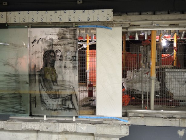 new art, pictures of people on the subway, on glass panels installed at Union Station platform - a seated woman picture on the left.  The panel on the right has not yet been installed, there is a space and the construction behind it is easily visible