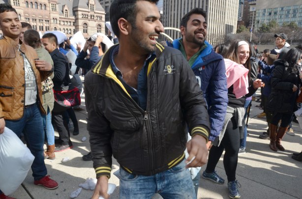 four young men laughing as they partake in a pillow fight. 