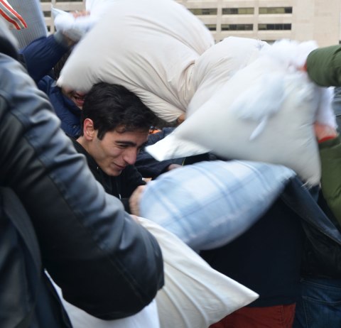 A young man being overwhelmed a bit by a large number of pillows being aimed his way. 