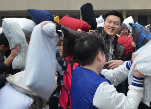 Young men swinging pillows at each other and trying to hit each other, all in good fun. 