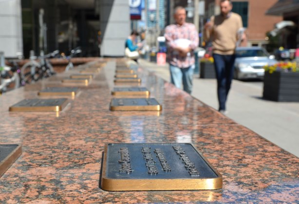  Along the top of the wall are plaques with names of people who died in the workplace between 1901 and 1999.  The name, year and cause of death is given on each plaque.   View looking down the top of the wall. 