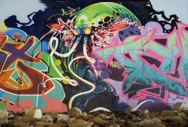 part of a mural under a bridge - large mantishrimp creature with long antennae (tentacles?) emerging from behind a tag
