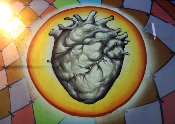 part of a mural on a concrete wall under a bridge under the 401 in Toronto, an anatomical painting of a heart that looks #D, surrounded by a yellow circle