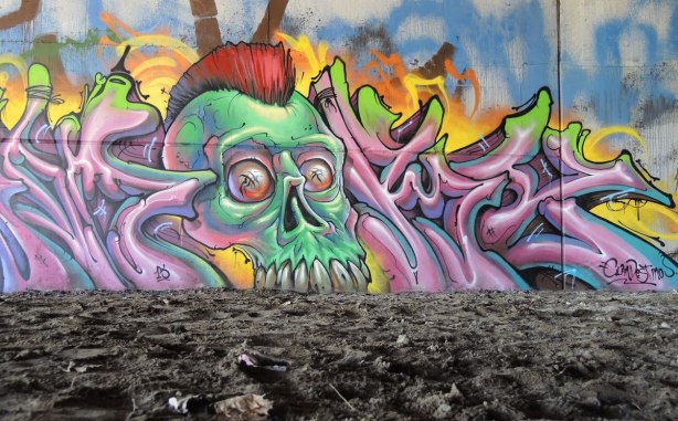mural painting on a wall, looks like a green zombie head coming out of the ground.  photo taken from a low angle 