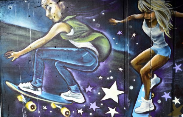street art painting under a railway bridge - a young man and a young woman on skateboards