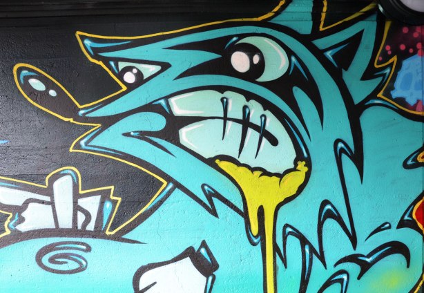 street art painting under a railway bridge - an ugly blue creature with nasty look on his face, yellow stuff oozing from the corner of his mouth 