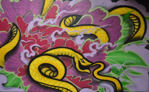 street art painting under a railway bridge - a long yellow snake curld up amongst purple and red swirls