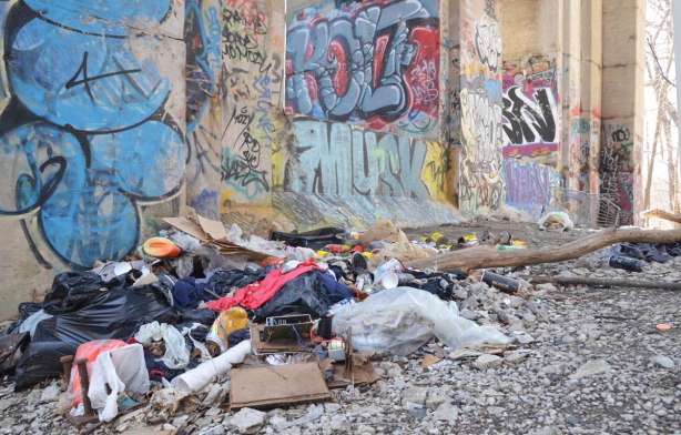 graffiti on the concrete supports under a bridge - a pile of trash beside graffiti covered sections of the bridge 