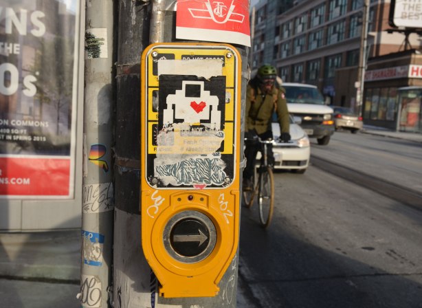 lovebot sticker on a yellow sign by the button one pushes when one wants to cross at a streetlight.