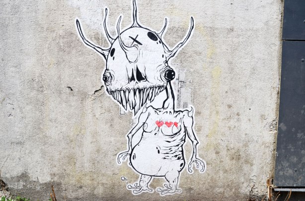 A grominator figure wheatpaste, black drawing on white, including body, arms and stubby little legs.  He has 3 lovebot hearts, 2 1/2 are red 