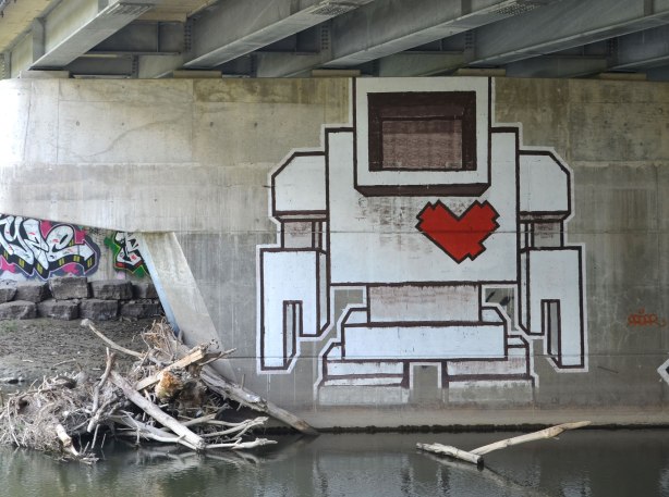 A large lovebot on a concrete support under a bridge by a river
