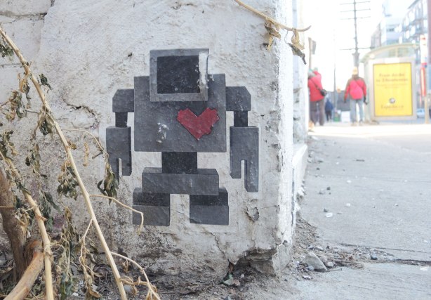 grey lovebot wheatpaste on a wall on Ossington Ave., it's down low so some dead weeds are nearby