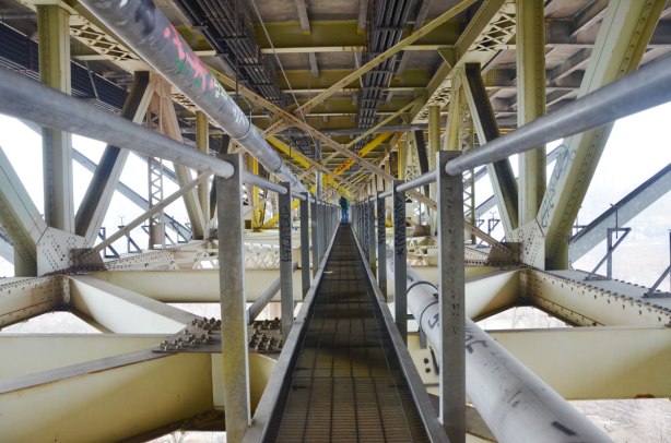 Catwalk under the Millwood bridge, looking down almost the whole length of it. A person is on the catwalk in the distance.