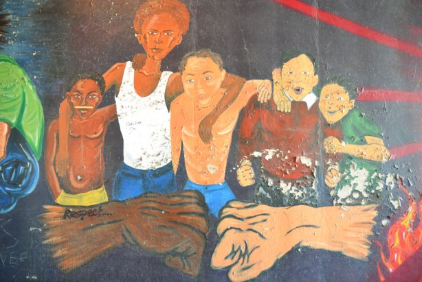 part of an old mural where the paint is starting to peel - a multiracial group of 5 young men also two fists coming together in the forground, one dark brown and one light brown. The word respect is written on one of the arms.